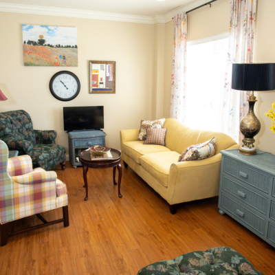 Living room area of one of our suite-size assisted living apartments. Our apartments have large windows with blinds included. This image shows our staged apartment to help you visualize how furniture can be placed in the space.